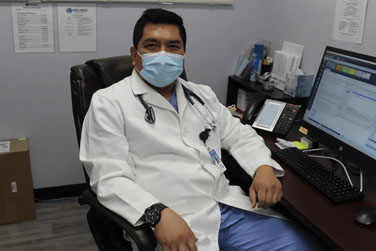 A doctor sitting in his office wearing a mask.