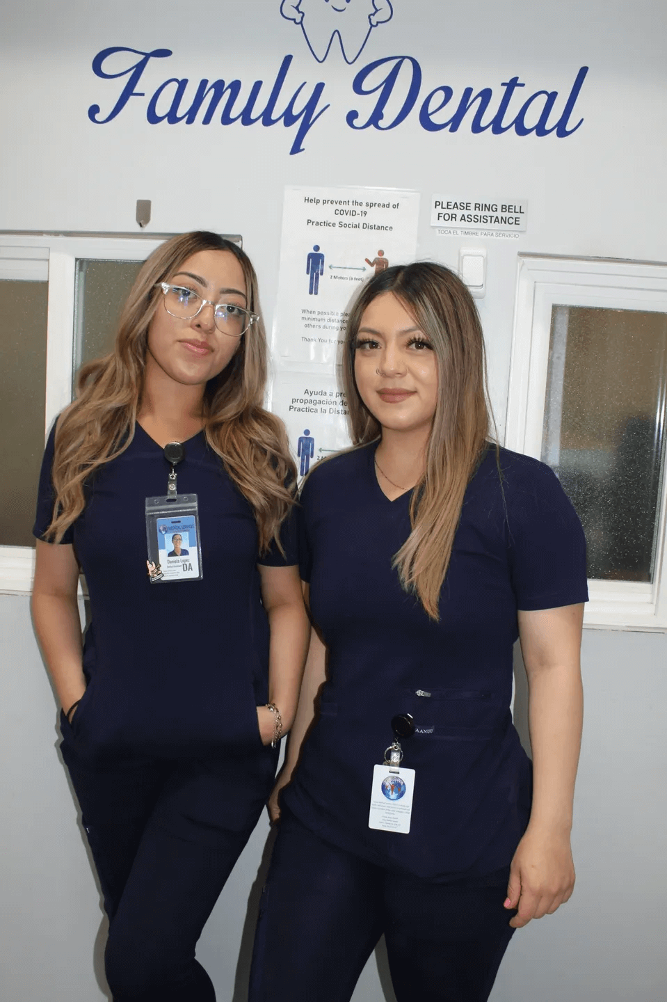 Two women in blue scrubs standing next to a wall.