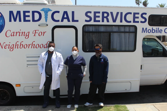 Three people standing in front of a medical service bus.