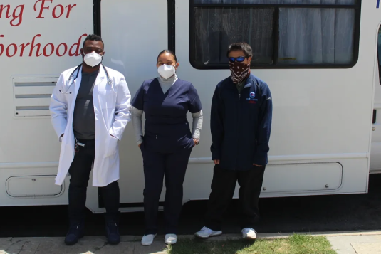 Three doctors stand in front of a bus.